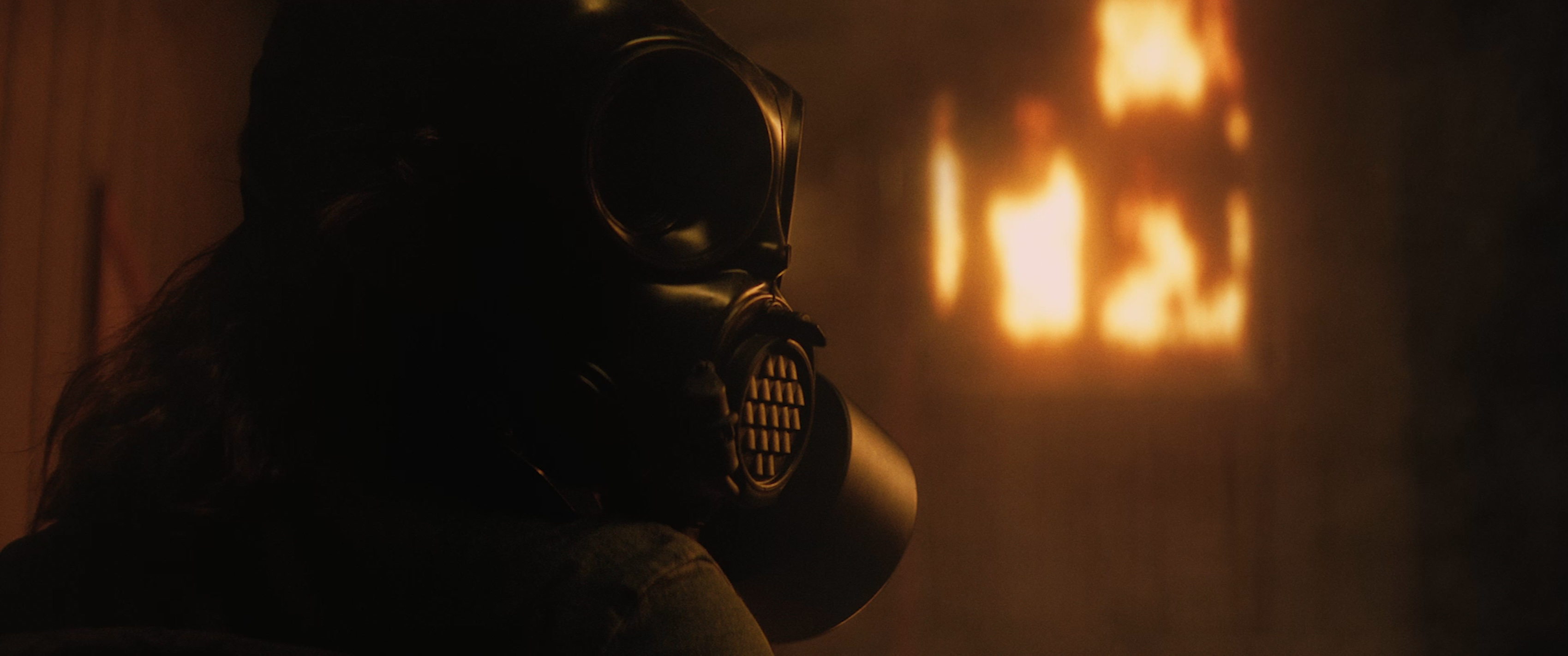 Still from the film, featuring a gas mask in the foreground and some sort of fire in the background.